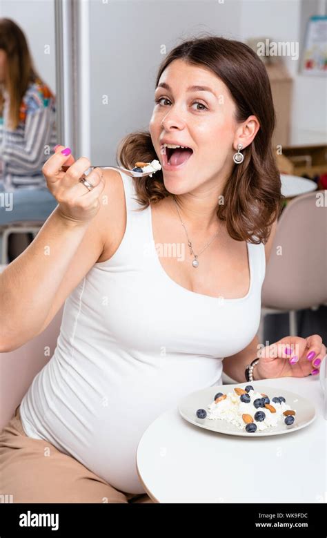 Portrait Of Young Pregnant Woman Wearing White Shirt Eating Cottage Cheese With Berries And Nuts