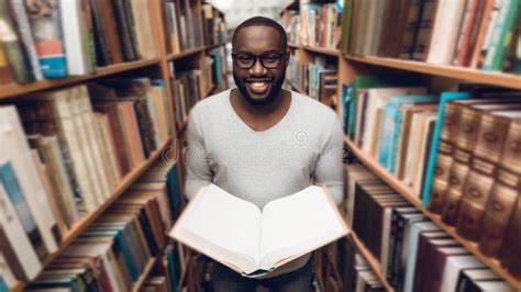 Ethnic African American Guy Reading Book Smiling In Aisle Of Library