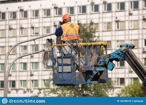Worker In Lift Bucket During Installation Of Metal Pole With Street