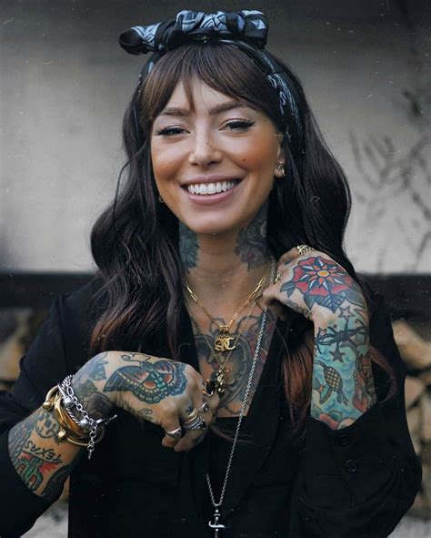 a woman with many tattoos on her arm and chest smiling at the camera while wearing a black shirt