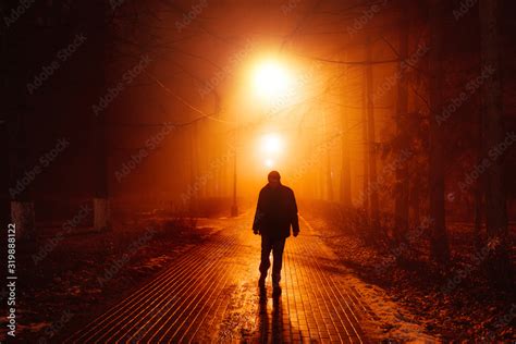 Sad Man Alone Walking Along The Alley In Night Foggy Park Front View