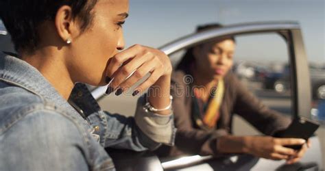 Two Black Women Friends Leaning Against Car Talking And Texting Stock