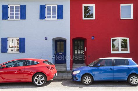 A Red And A Blue Car Parking In Front Of A Blue And A Red House