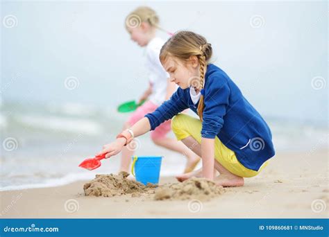 Two Little Sisters Having Fun On A Sandy Beach On Warm And Sunny Summer