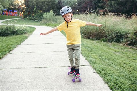 여름날 공원의 도로에서 스케이트보드를 타는 회색 헬멧을 쓴 행복한 백인 소년 계절에 따라 야외 어린이 활동 스포츠 건강한 어린 시절의 생활 방식 스케이트 보드를 타는