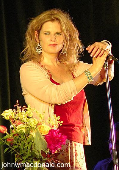 A Woman Holding A Microphone On Stage With Flowers In Front Of Her And