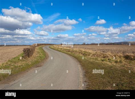 A Quiet Country Road Winding Through Hedgerows And Newly Plowed Fields