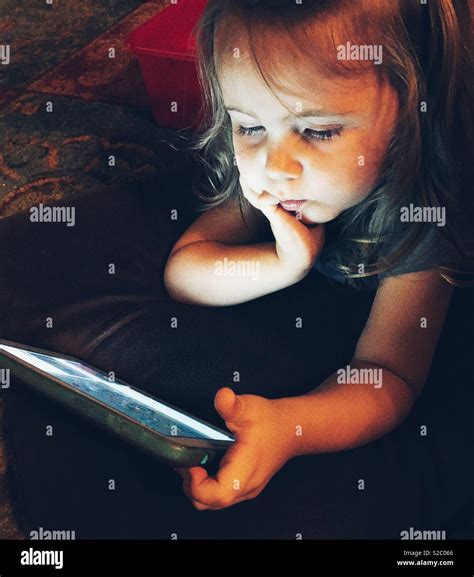 Toddler Girl Laying On Floor In The Dark Playing With Tablet Stock