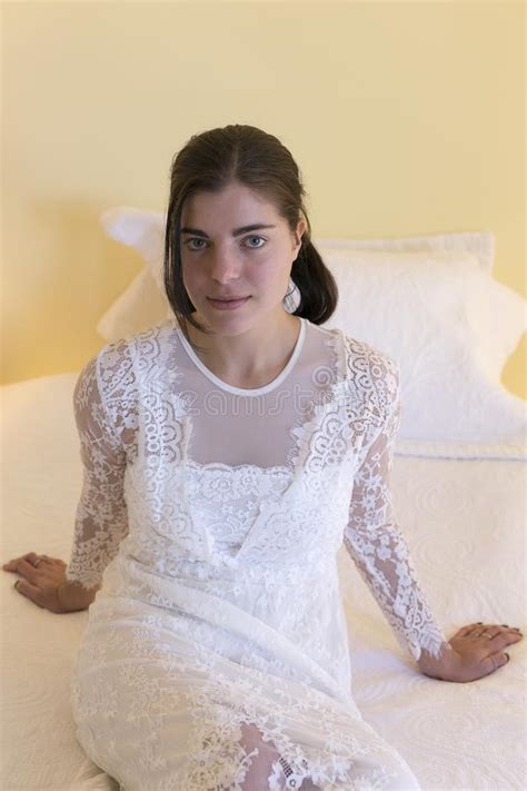 Brunette Girl Wearing Long White Lace Dress Sitting On Bed Stock Image