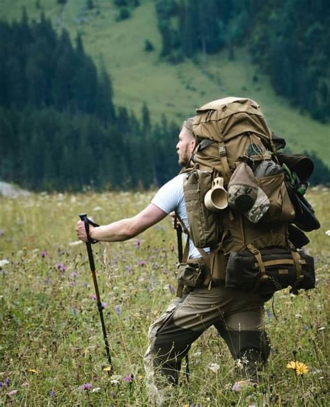 A Man With A Backpack And Hiking Poles Walks Through The Grass