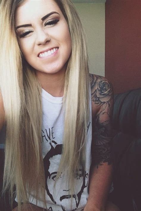 A Woman With Long Blonde Hair And Tattoos On Her Arm Smiling At The Camera