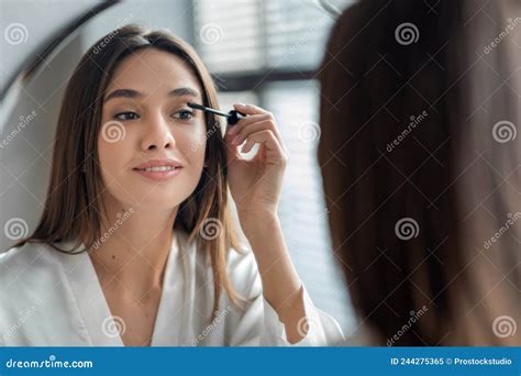 Beautiful Millennial Lady Doing Daily Makeup Near Mirror In Bathroom Applying Mascara Stock