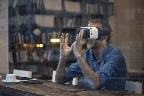 Geschäftsmann Der Einen Virtual Reality Simulator Trägt Und Am Tisch Sitzt Lizenzfreies Stockfoto