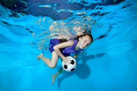 Счастливая маленькая девочка плавает и играет под водой с футбольным
