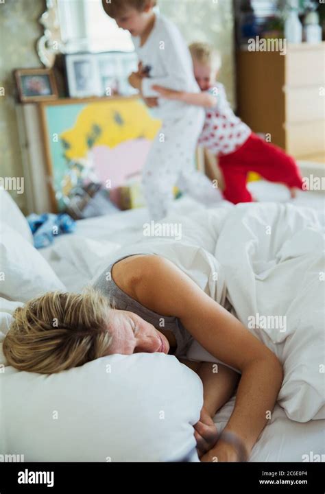 Mother Sleeping In Bed While Her Sons Playing In Background Stock Photo