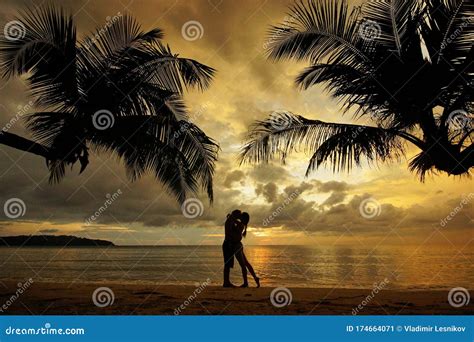 Silhouette Of Kissing Couple Standing On Tropical Beach During Sunset