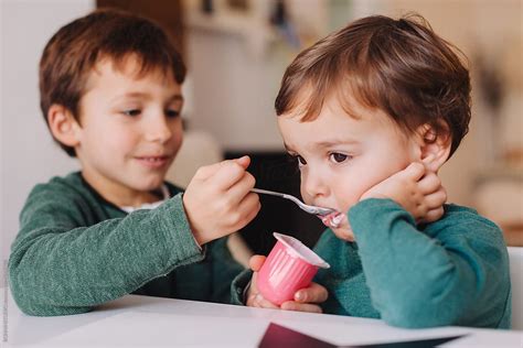 Young Boy Helping His Little Brother To Eat A Strawberry Yoghurt Del