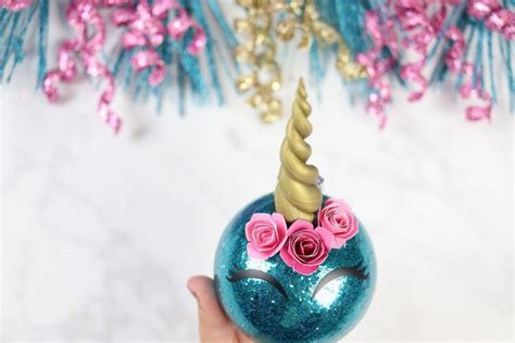 A Hand Holding A Blue Ornament With A Pink Rose On Its Face