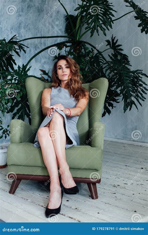Portrait Of A Beautiful Fashionable Woman In A Gray Dress Sitting In A Green Chair Stock Image