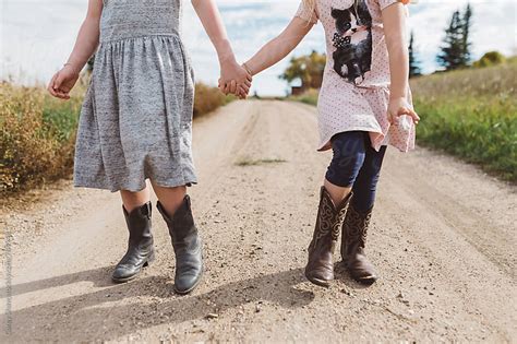 Young Sisters Wearing Cowboy Boots And Holding Hands By
