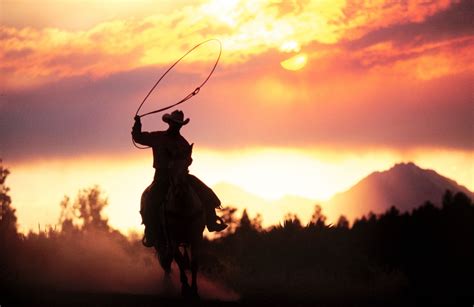 Cowboy On Horseback With Lasso In The Air And Dust Flying At Sunset
