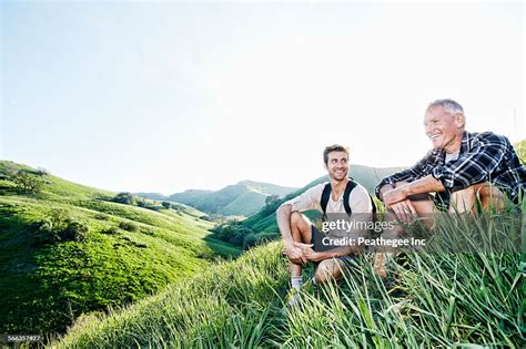 Caucasian Father And Son Sitting On Grassy Hillside High Res Stock