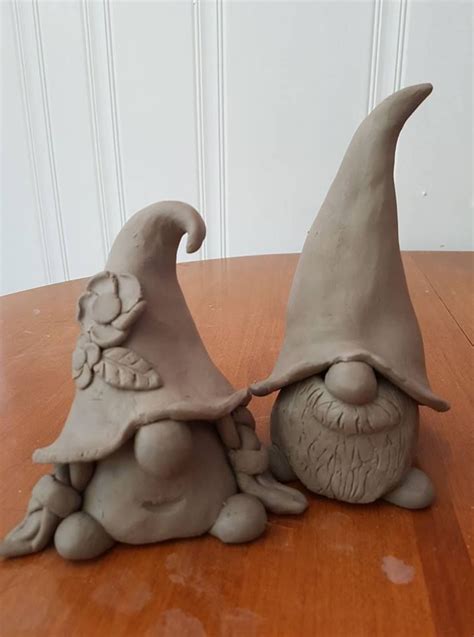 Two Clay Gnomes Sitting On Top Of A Wooden Table