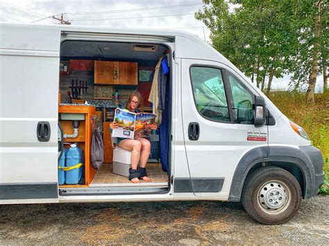 A Woman Sitting In The Back Of A Van Reading A Magazine