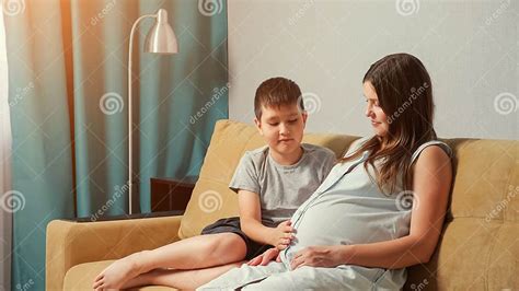 Pregnant Mom And Son On The Couch Boy Stroking And Hugging Belly Stock