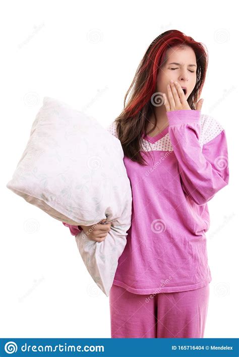 Tired Young Girl In Pajamas Holding A Pillow And Yawning Stock Photo
