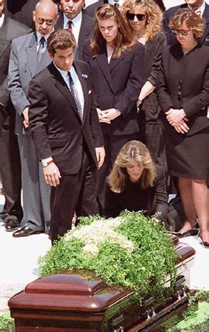 A Group Of People Standing Around A Woman Laying Her Head On The Ground In Front Of A Casket
