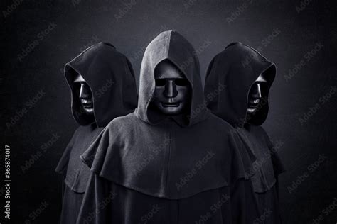 Group Of Three Scary Figures In Hooded Cloaks In The Dark Stock Photo