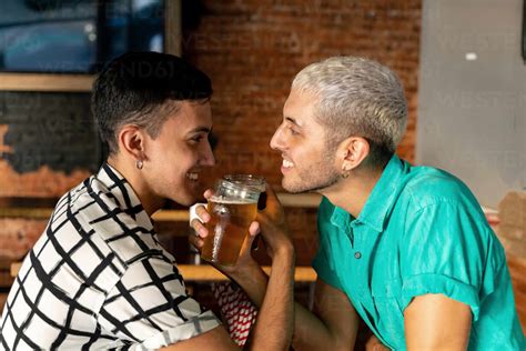 Romantic Gay Couple Enjoying Drinking Beer With Arm In Arm At Bar Stock