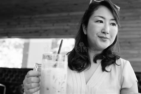 Mature Asian Woman Relaxing At Coffee Shop While Thinking Stock Image