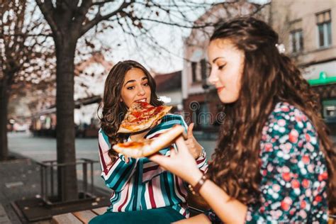Two Cheerful Girl Talking And Eating Pizza Outdoors Having Fun