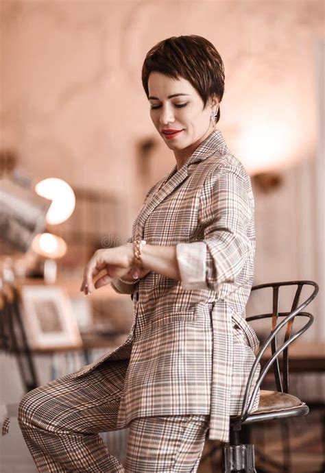 Short Haired Brunette Woman In Elegant Business Plaid Pantsuit With Rolled Up Sleeves Sits On A