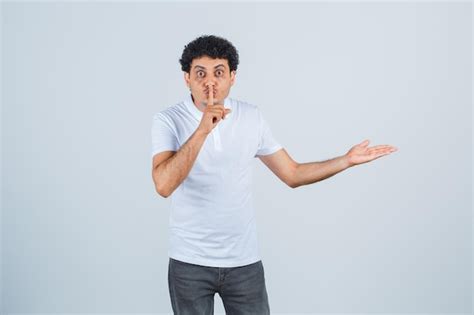 Free Photo Young Male In White T Shirt Pants Showing Something And Silence Gesture And