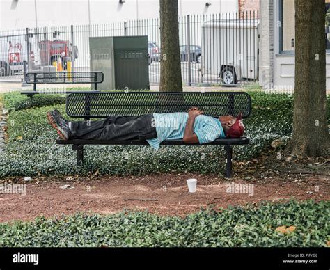 Homeless African American Or Black Man Sleeping On A Park Bench In