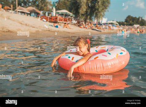 glückliche kleine mädchen spielen mit aufblasbaren ring in wasser an heißen sommertag kinder