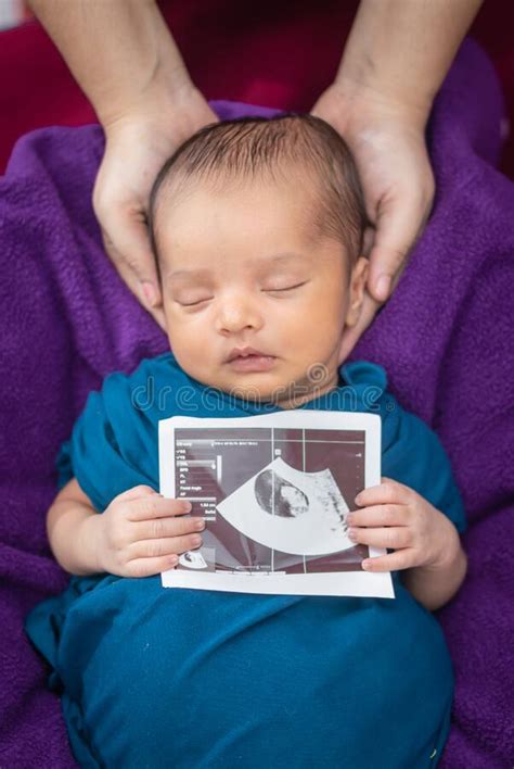 Newborn Baby Holding Ultrasound Copy In Hand And Sleeping In Baby Wrap