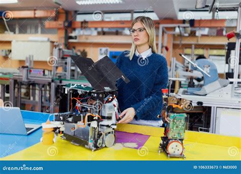 Young Beautiful Female Engineer Testing Robot In Workshop Stock Image