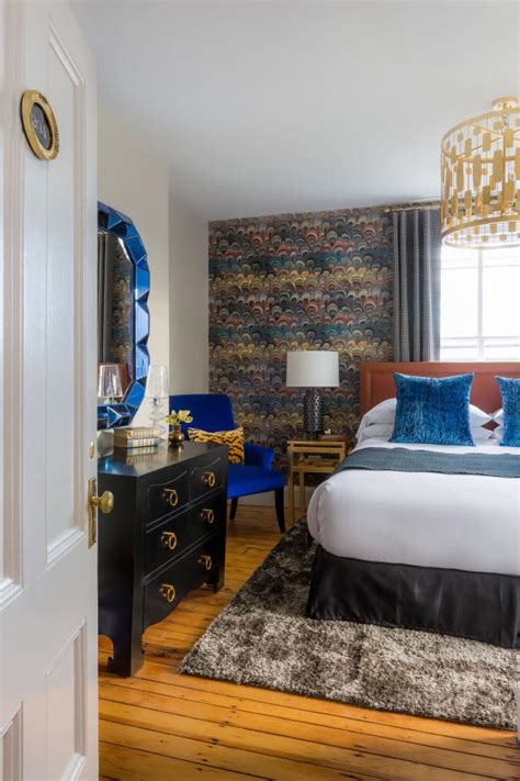 A luxurious blue home office with bright walls, a round desk, white furniture, a quirky chandelier, an acrylic bench with faux fur. Eclectic Bedroom With Royal Blue Accents & Feather Design Accent Wall | HGTV