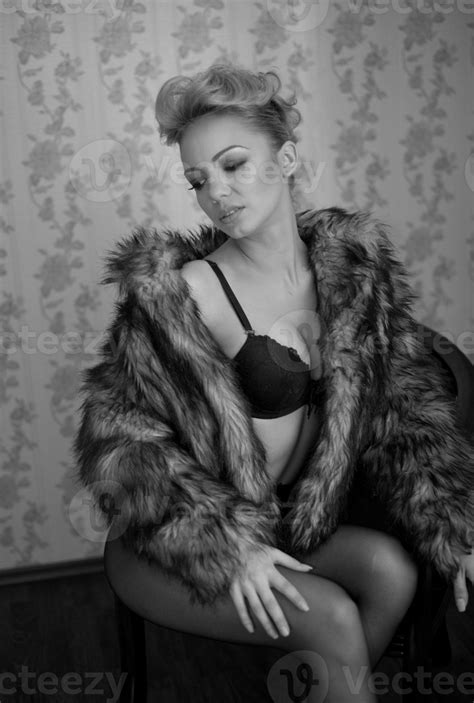 attractive blonde model with pantyhose black bra and fur coat posing provocatively on chair