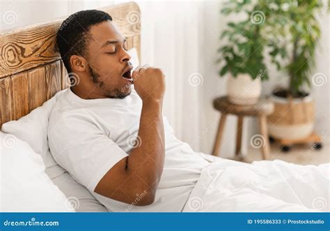 Sleepy African American Man Yawning Sitting In Bed At Home Stock Image