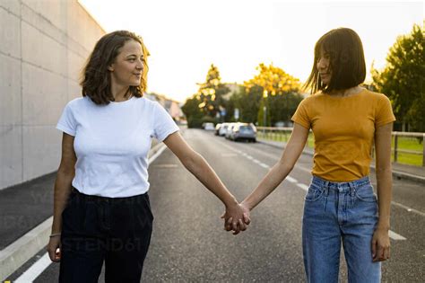 Young Lesbian Couple Looking At Each Other While Holding Hands On Road