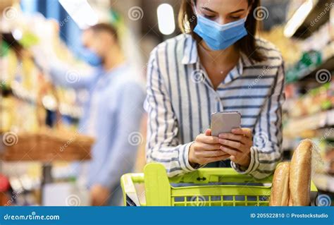 Young Woman In Mask With Phone Shopping In Hypermarket Stock Photo