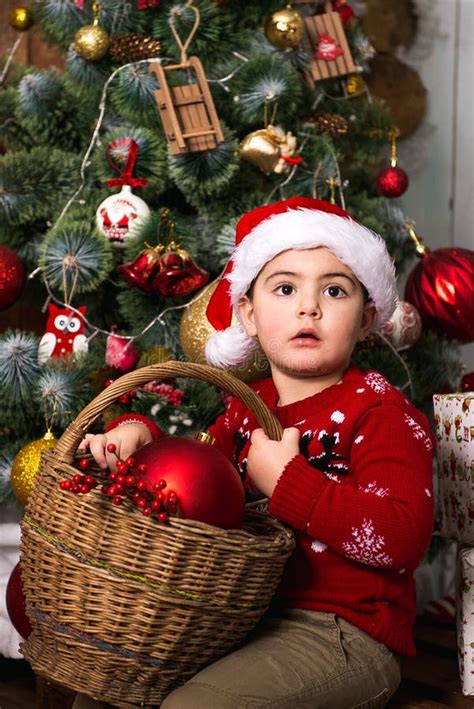 Little Boy In Santa Hat Decorates Christmas Tree With Red Toys Stock