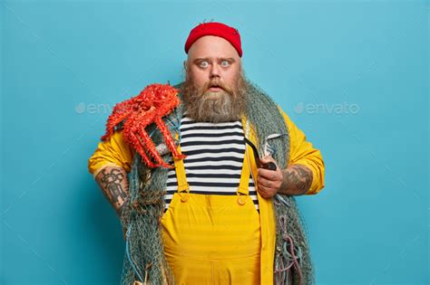 Stupefied Bearded Man Stares Bugged Eyes At Camera Holds Pipe Dressed In Yellow Overalls Red Hat
