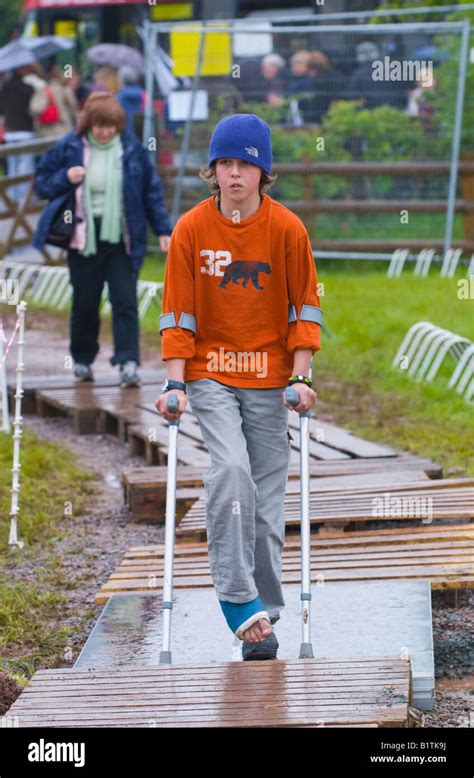 Teenage Boy On Crutches Crossing Duckboards Over Mud At Entrance To