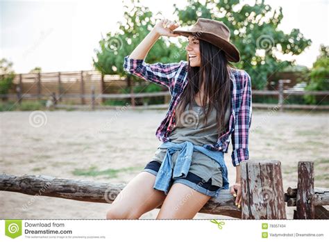 Cheerful Relaxed Young Woman Cowgirl Sitting On Fence And Smiling Stock